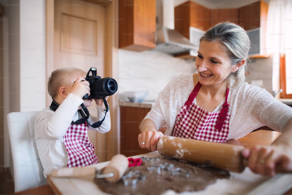 A handicapped down syndrome boy taking photos with a digital camera and his mother indoors in a kitchen baking.