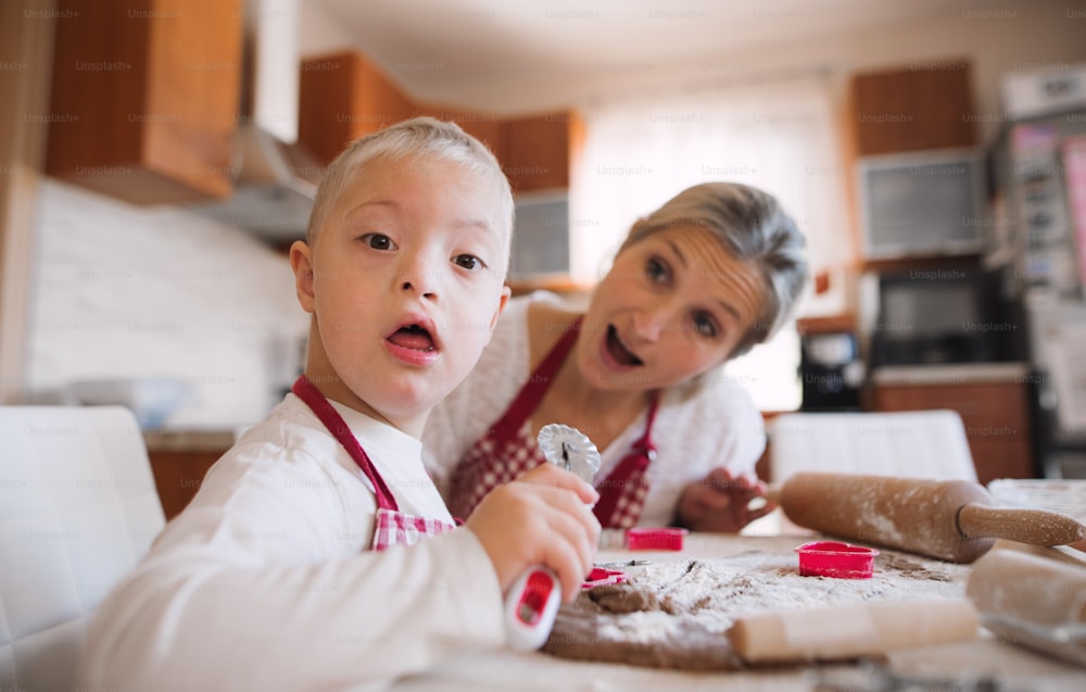 A handicapped down syndrome boy and his mother with checked aprons indoors baking in a kitchen.