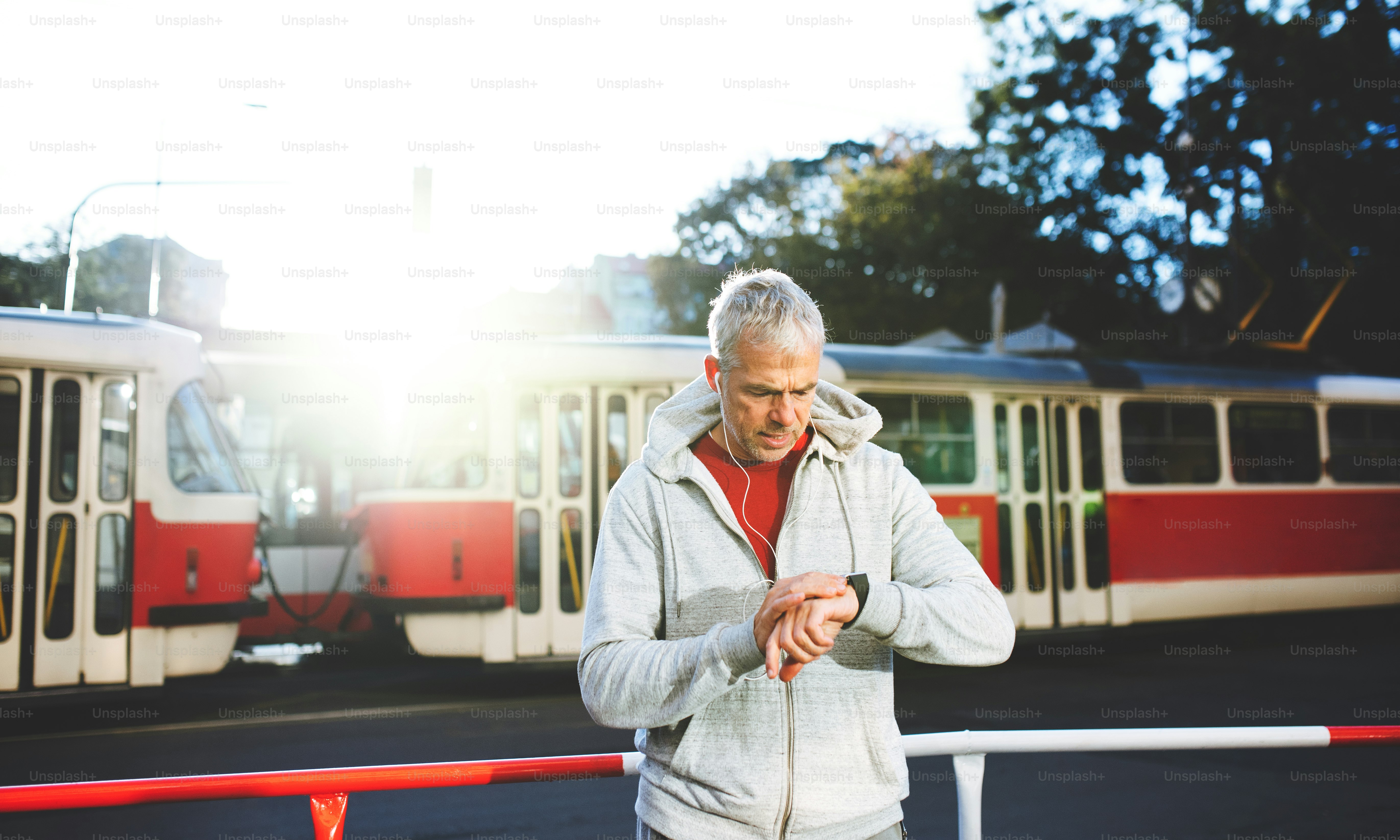 Un retrato de un hombre maduro activo con auriculares parado al aire libre en la ciudad, mirando la hora.