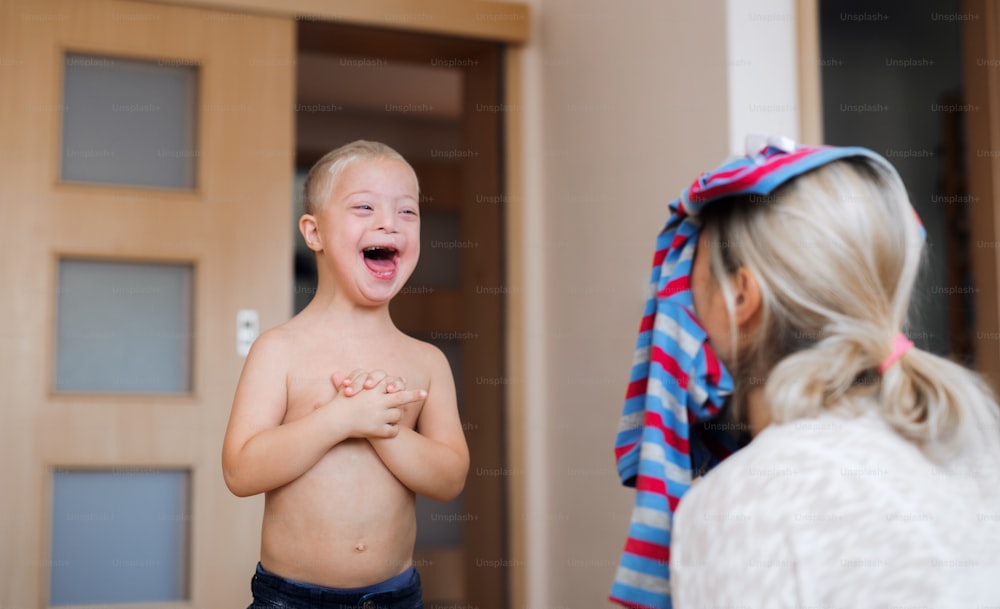 A laughing handicapped down syndrome boy playing with his unrecognizable mother indoors, having fun.