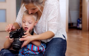 A handicapped down syndrome boy and his mother with a digital camera indoors, taking pictures.