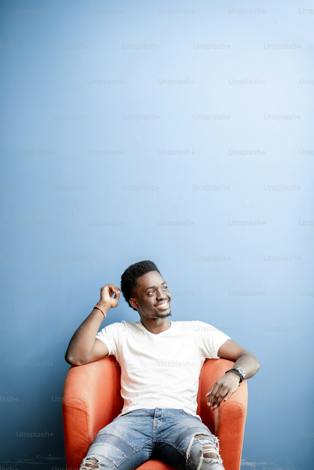 Portrait of a young african man dressed in white t-shirt and jeans sitting on the chair on the colorful background. Image with copy space