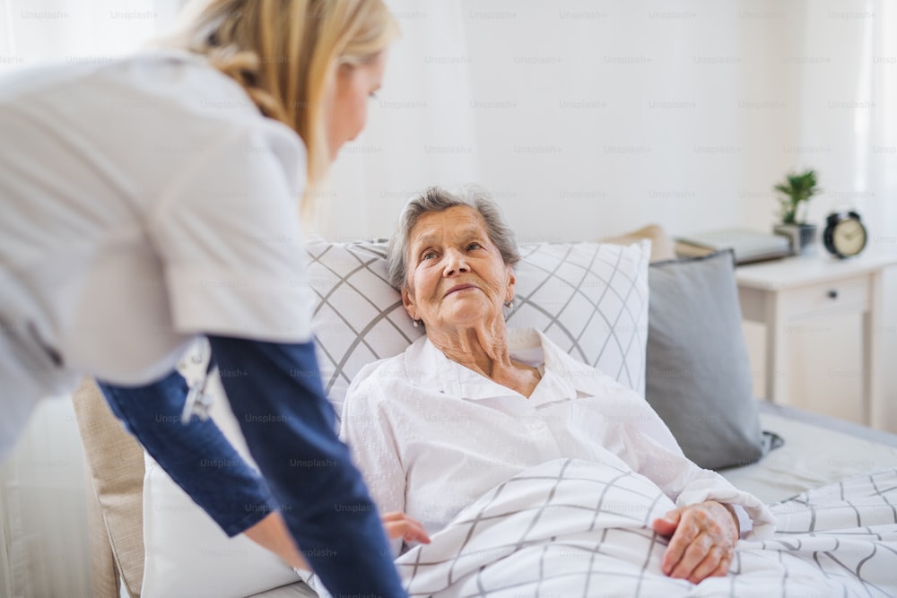Un giovane operatore sanitario che parla con una donna anziana malata felice sdraiata a letto a casa.