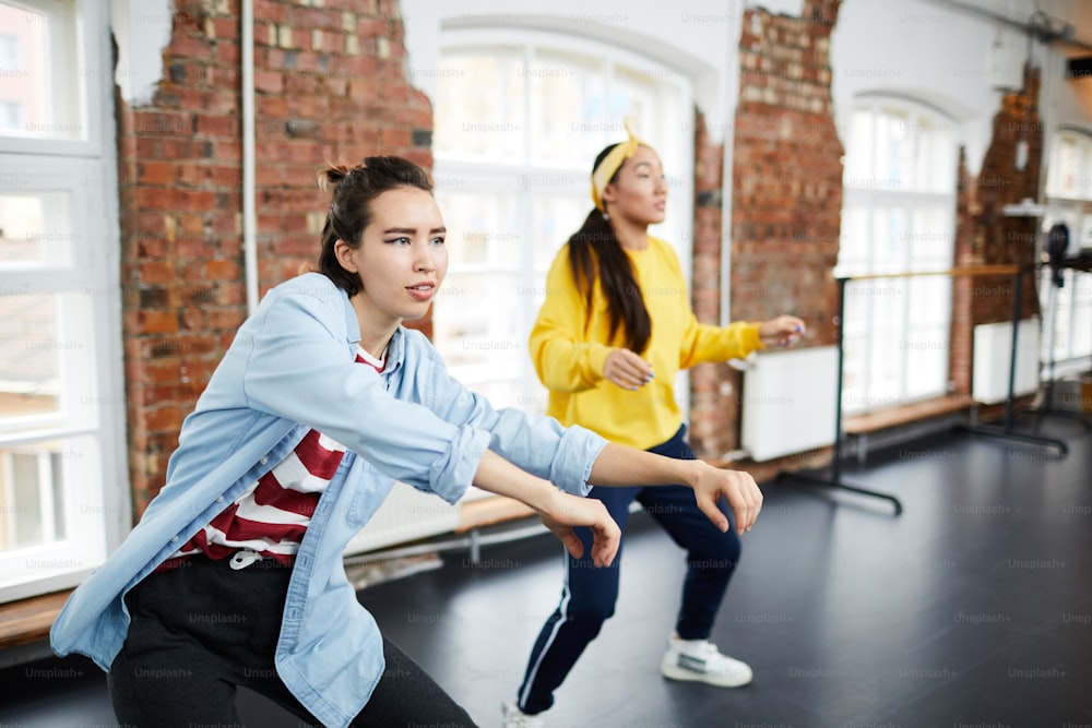 Young active woman and her groupmate learning hip hop dancing in modern studio
