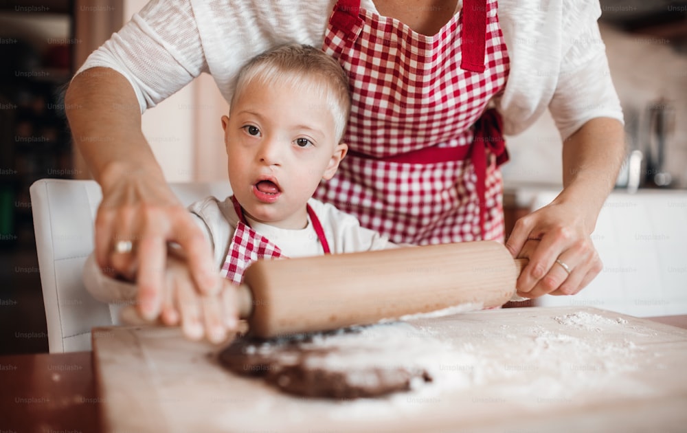 障害のあるダウン症の子供と、チェックのエプロンを付けた見分けのつかない母親が、室内でキッチンでパンを焼いている。