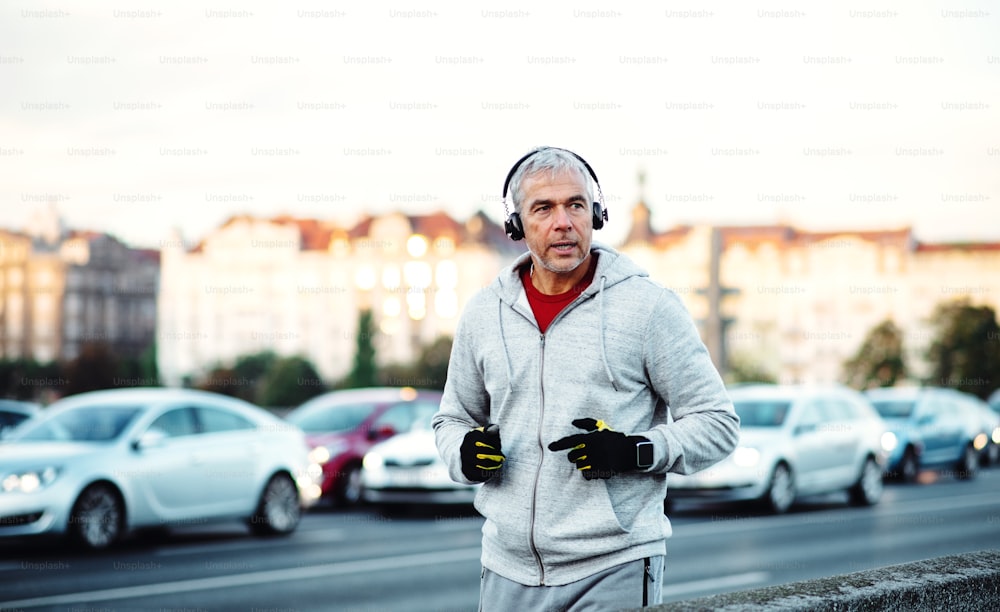 A fit mature male runner with headphones running outdoors on the bridge in Prague city, listening to music.