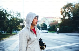 Mature male runner with water bottle standing outdoors in city, resting after the run.