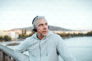 Mature male runner with black headphones outdoors on the bridge in Prague city, listening to music.