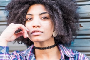 Close up portrait of a beautiful black woman smiling and looking at you. Hipster shirt and clothes for young teenager woman with attractive eyes and afro hair. urban background