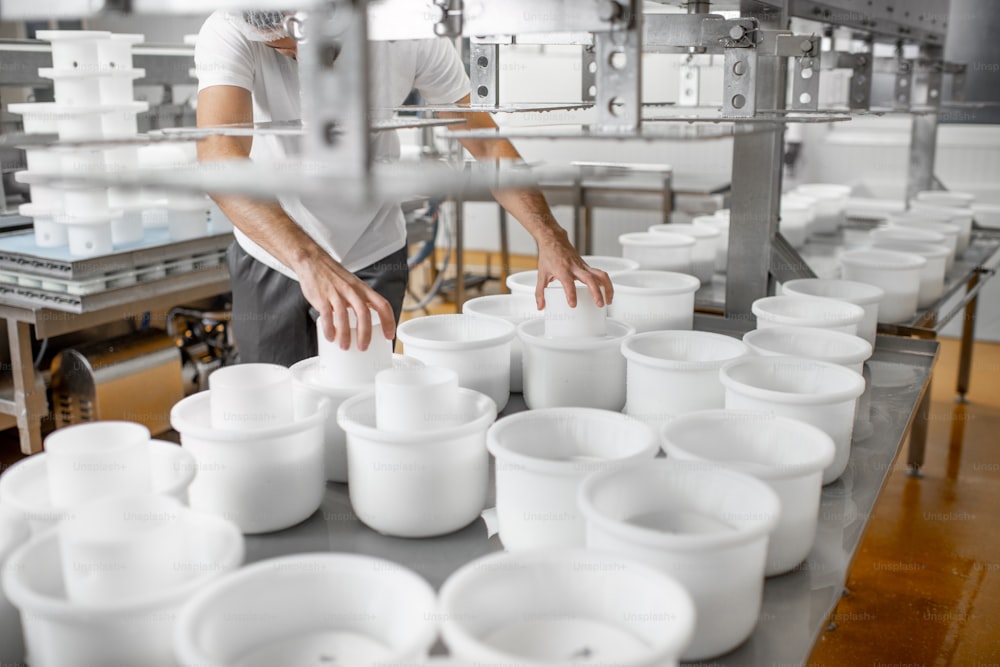 Homem uniformizado formando queijo nos moldes de plástico colocando-os sob a prensa na fabricação de queijo