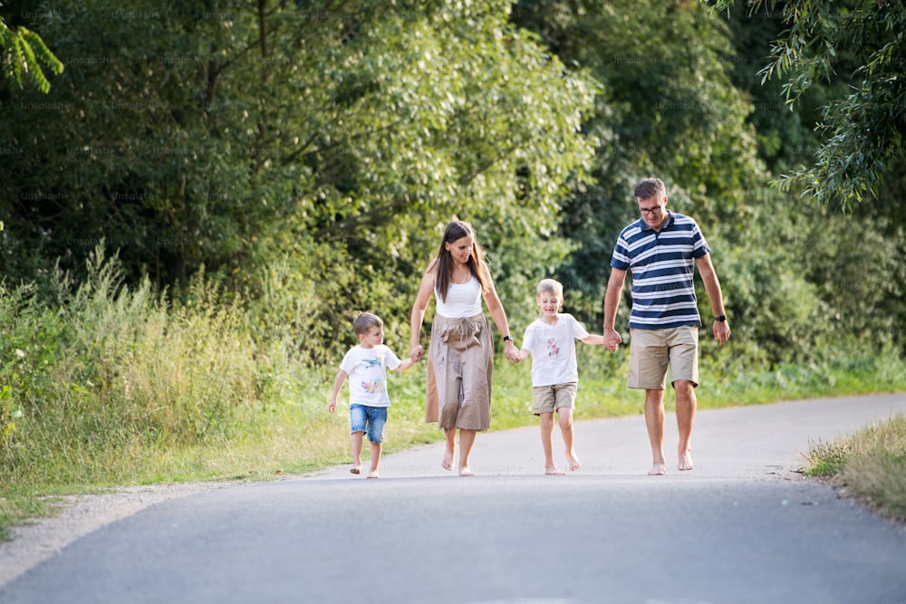 Eine junge Familie mit zwei kleinen, fröhlichen Söhnen, die an einem Sommertag barfuß auf einer Straße im Park laufen und Händchen halten.