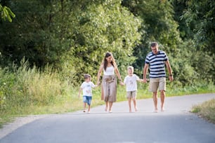 Una familia joven con dos hijos pequeños y alegres caminando descalzos por una carretera en un parque en un día de verano, tomados de la mano.