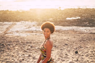 Bela pele afro pele raça senhora na praia com pôr do sol e luz de fundo em fundo desfrutando de atividade de lazer ao ar livre. Vestido tradicional estilo afro e cores. Modelo preto bonito