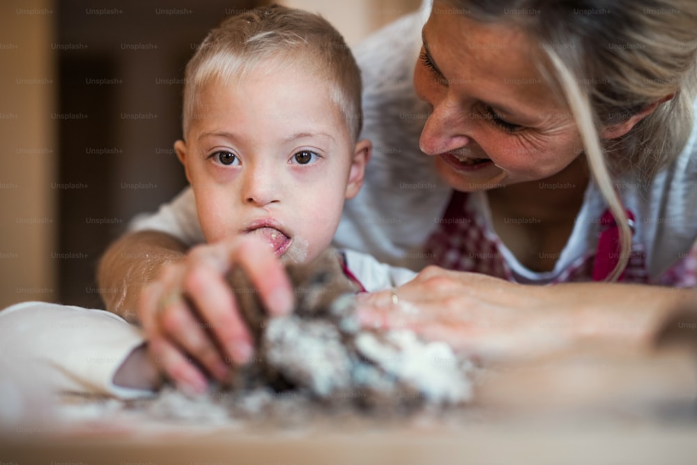 Un enfant handicapé trisomique heureux et sa mère à l’intérieur en train de cuisiner dans une cuisine.
