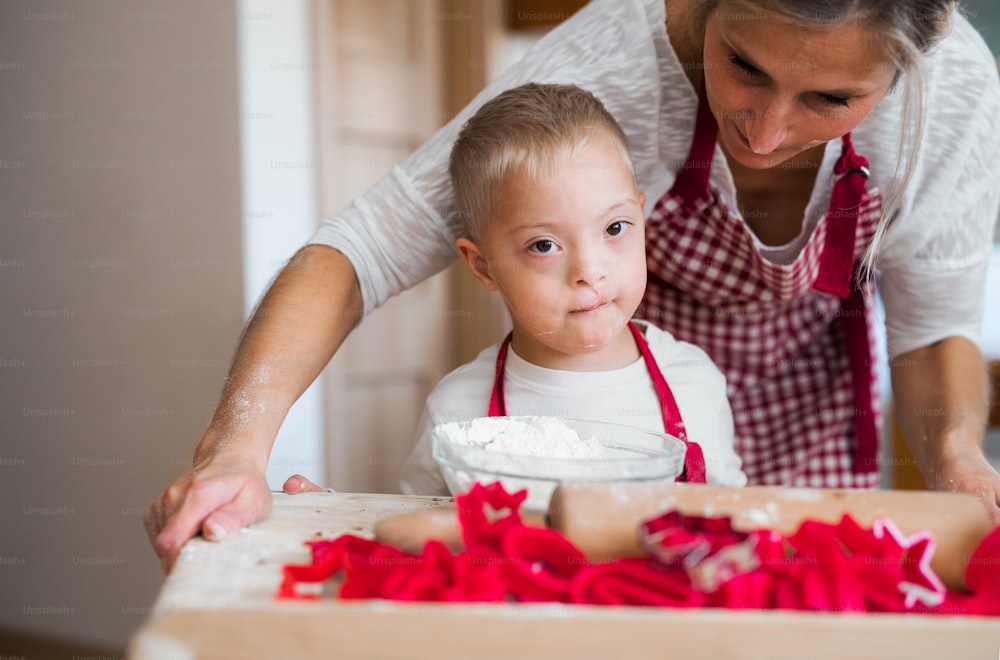 A happy handicapped down syndrome child and his mother indoors baking in a kitchen.