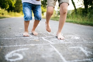 Legs of two barefoot unrecognizable small boys hopscotching on a road in park on a summer day.