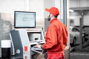 Trabalhador de serviço de carro em pneus de balanceamento de uniforme vermelho trabalhando com computador no serviço de montagem de pneus