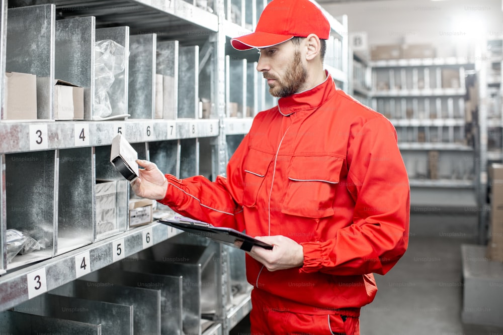 倉庫で商品をチェックする赤い制服を着た倉庫作業員が書類を記入しています