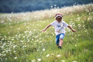 Um menino pequeno com óculos de piloto e chapéu correndo na natureza em um dia de verão. Espaço de cópia.