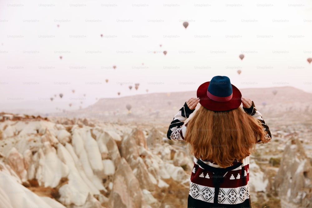 Reise. Schöne Frau mit Hut beobachtet fliegende Heißluftballons vom Hügel aus. Weiblich in ethnischer Kleidung in Kappadokien. Hohe Auflösung