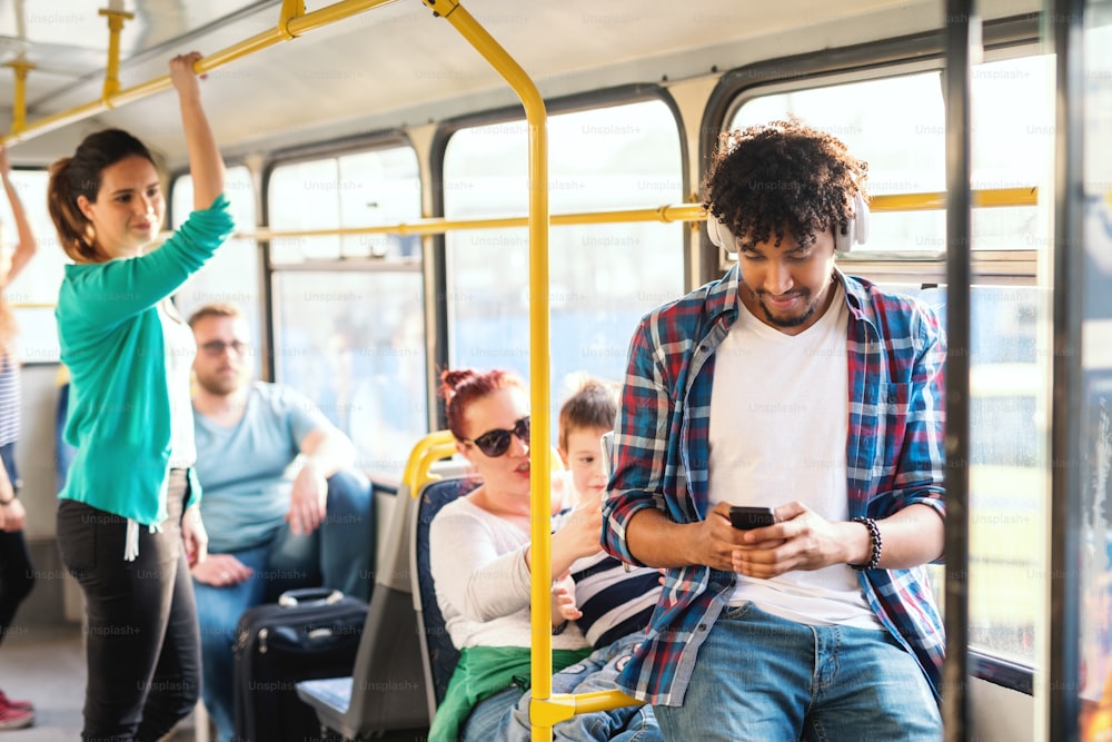 Junger Afrikaner, der Musik hört und Smartphone benutzt, während er in öffentlichen Verkehrsmitteln fährt.