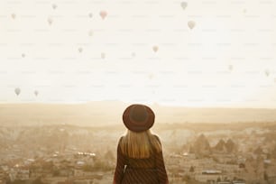 Voyager. Belle femme en chapeau sur la colline avec des montgolfières volantes dans le ciel. Femme voyageant en Cappadoce. Haute résolution