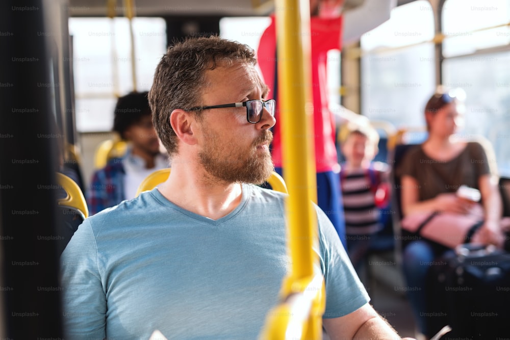 Close up do homem caucasiano com óculos olhando para o lado enquanto está sentado no ônibus da cidade.
