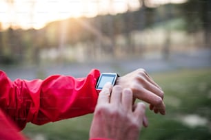 A midsection view of hands of female runner with smartwatch outdoors in autumn nature, checking the time.