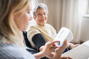 Un joven visitador de salud mide la presión arterial de una mujer mayor en silla de ruedas en su casa.