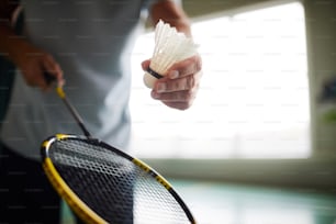 Jogador de badminton segurando raquete e peteca enquanto vai arremessar e acertá-lo no início do jogo