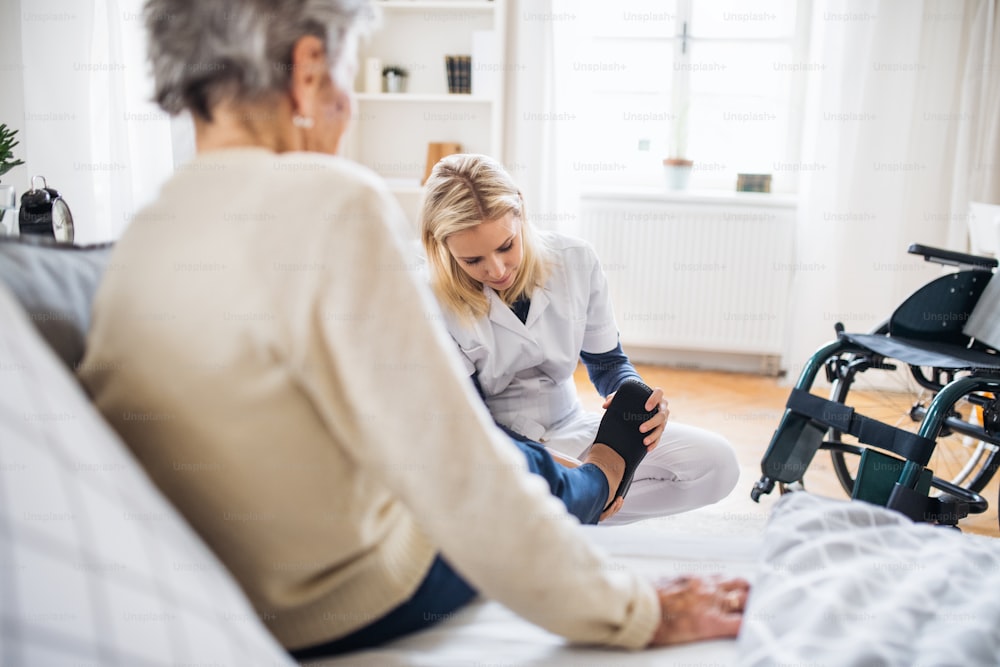 Un joven visitador de salud poniéndole pantuflas a una mujer mayor en su casa.