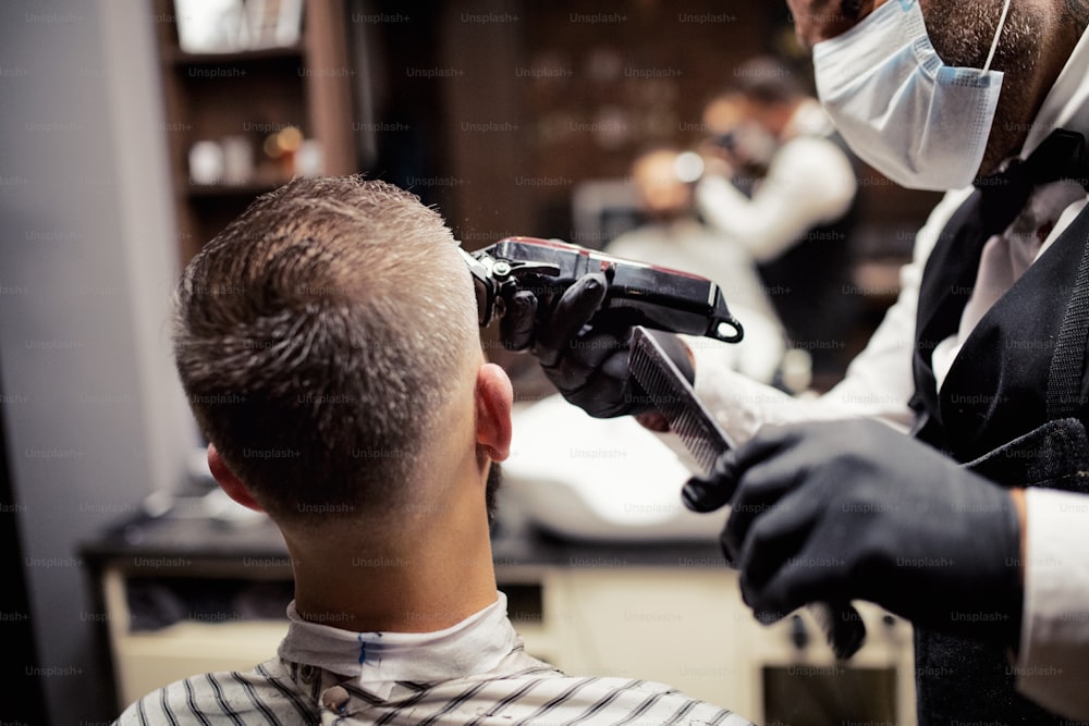 Rear view of handsome hipster man client visiting haidresser and hairstylist in barber shop.