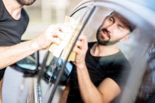Laveuse professionnelle essuyant une vitre de voiture avec une éponge jaune, lavant une voiture de luxe à l’extérieur