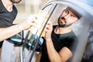 Professional washer wiping a car window with yellow sponge, washing luxury car outdoors