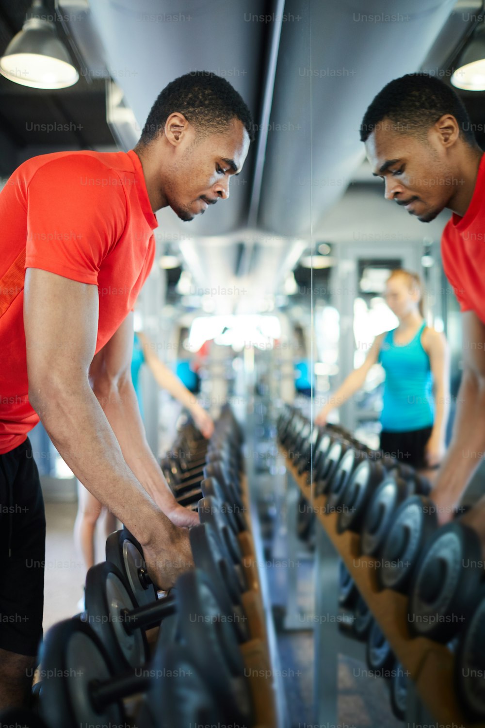 Young athlete taking two heavy barbells from row in front of mirror before exercising in fitness center