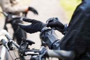 Eine Nahaufnahme eines Radfahrers mit Elektrofahrrad, der schwarze Handschuhe im Freien im Park anzieht.