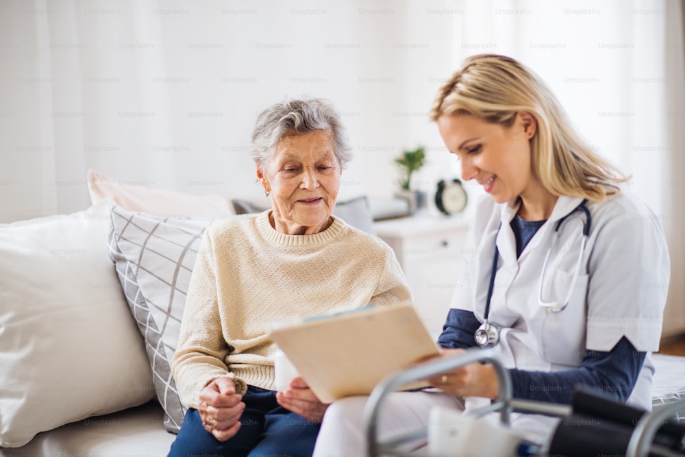 Un giovane operatore sanitario e una donna anziana seduta su un letto di casa, che parlano.