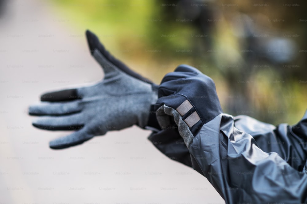 A close-up of a cyclist putting on black gloves outdoors in park.