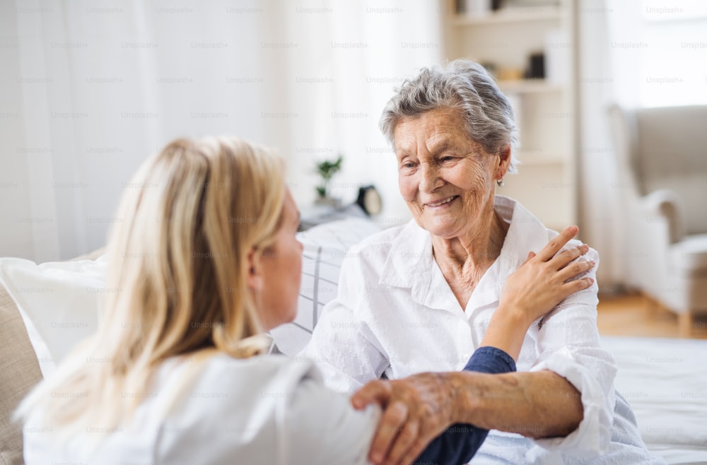 Un giovane operatore sanitario che parla con una donna anziana malata felice seduta sul letto di casa.