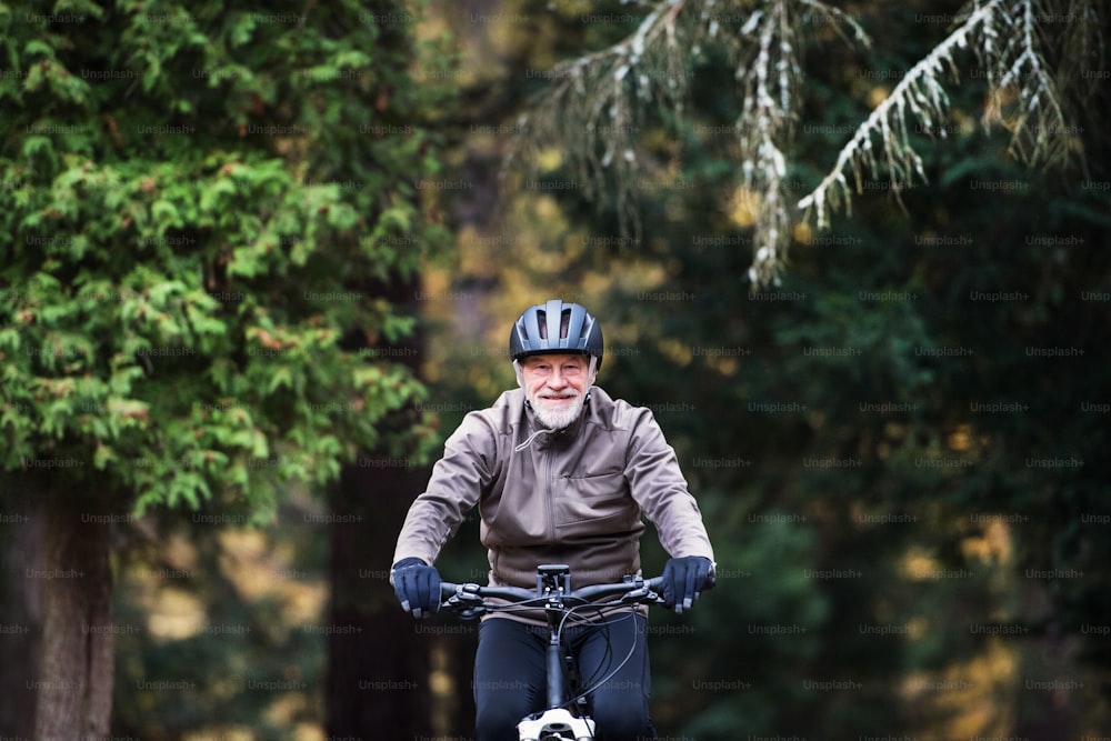Um homem idoso ativo com capacete e bicicleta de eletrocicleta ao ar livre em uma estrada na natureza.