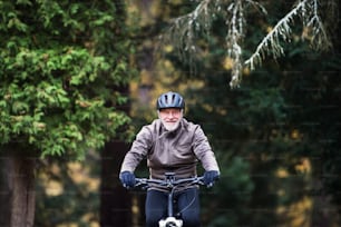 헬멧과 전기 자전거를 타고 자연 속에서 야외에서 자전거를 타는 활동적인 노인.
