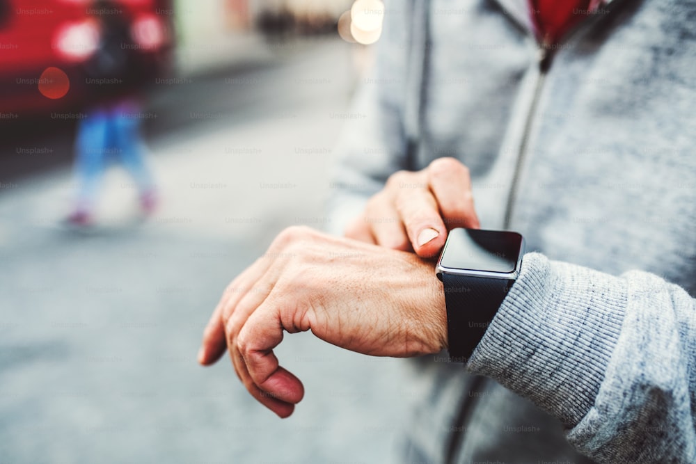 Un primo piano di mani di un uomo irriconoscibile in piedi all'aperto in città, utilizzando lo smartwatch.