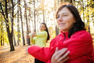 Two active female runners stretching outdoors in forest in autumn nature after the run.
