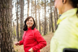 Two female runners with earphones jogging outdoors in forest in autumn nature, talking.
