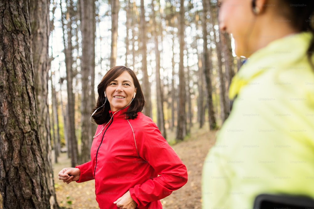 Deux coureuses avec des écouteurs font du jogging à l’extérieur dans la forêt dans la nature d’automne, en train de parler.