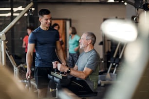 Un hombre mayor con un joven entrenador masculino haciendo ejercicios de entrenamiento de fuerza en el gimnasio.