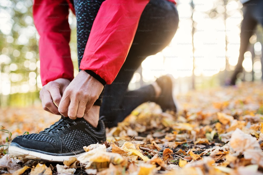A midsection view of hands of female runner outdoors in autumn nature, tying shoelaces.