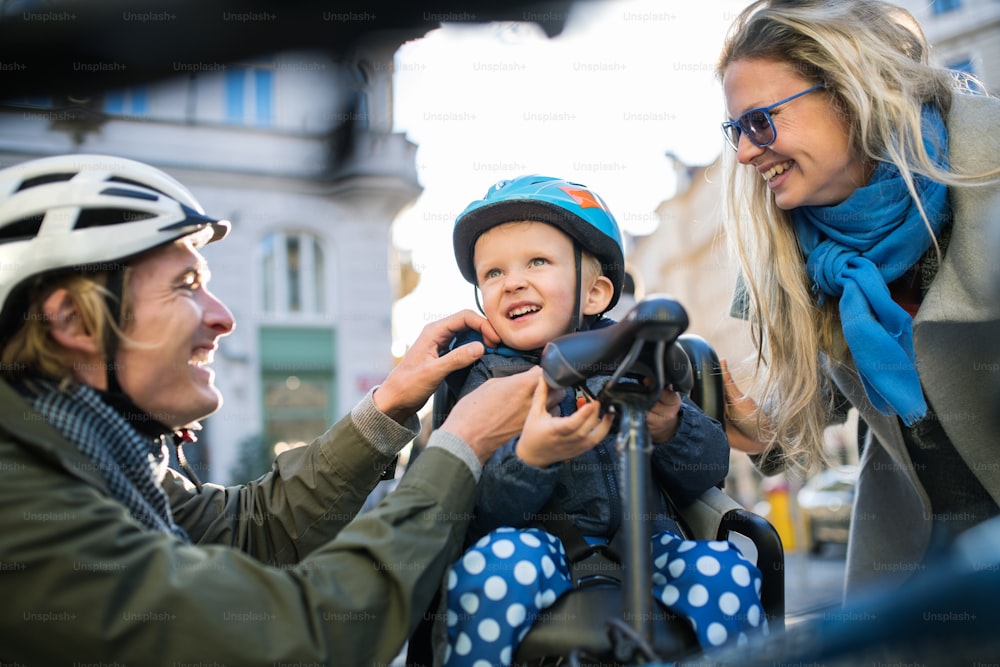 Un piccolo bambino con casco da bicicletta e giovani genitori all'aperto in città.