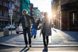 Un piccolo bambino con i genitori che attraversano una strada all'aperto in città al tramonto, tenendosi per mano.