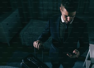 Vue de dessus d’un homme d’affaires en costume debout dans la chambre à coucher, tenant une valise et utilisant un téléphone intelligent. Concept de voyage d’affaires.